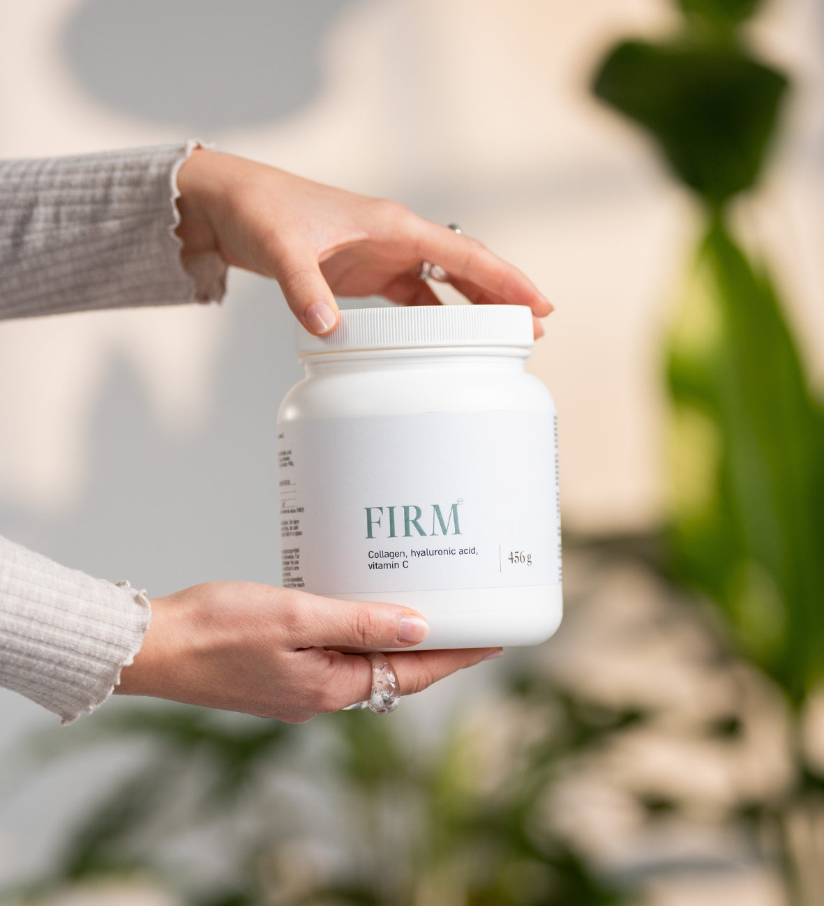 Hände halten eine weisse Dose „Firm“ mit Kollagenpulver.