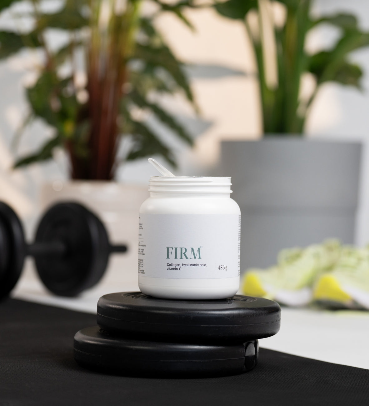 Weisse Dose „Firm“ mit Kollagenpulver auf Fitnessgewichten.