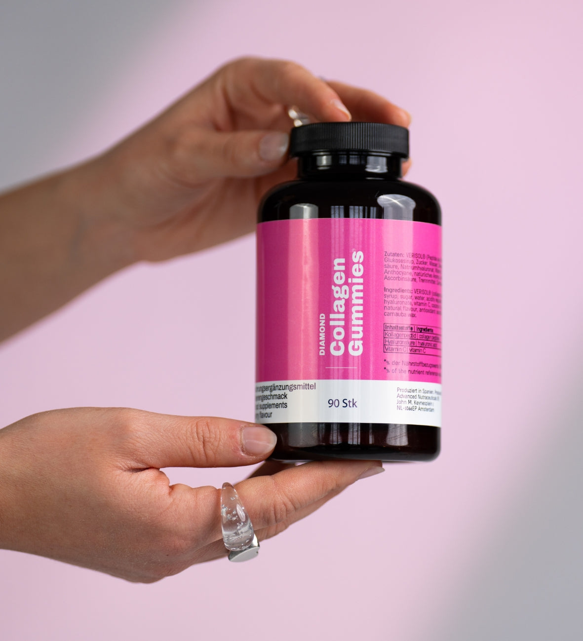 Hände halten eine Dose „Collagen Gummies“ vor rosafarbenem Hintergrund.