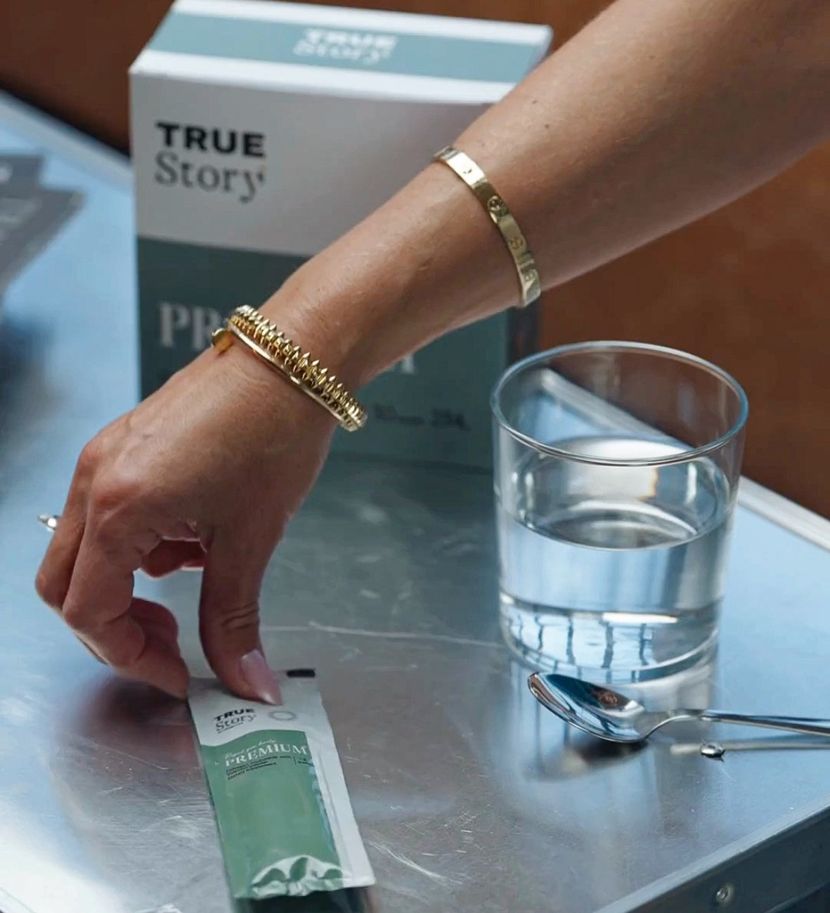 Hand greift nach einem „Premium“ Kollagen Sachet neben Glas Wasser.